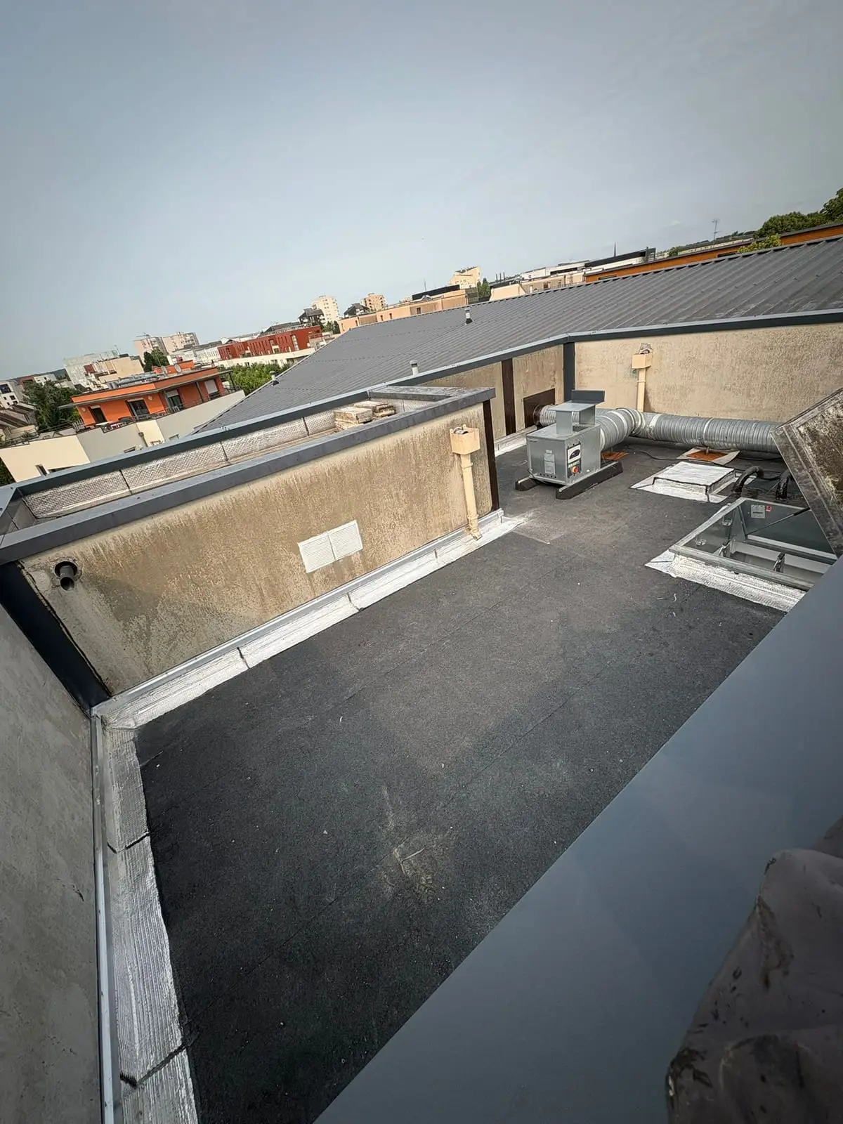 Terrasse technique rénovée en bitume entre deux versants de toiture zinc